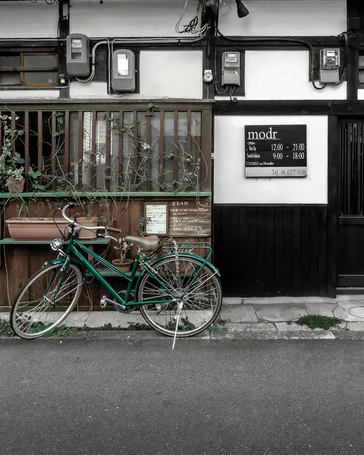 blue and green bicycle parked beside brown wooden house during daytime